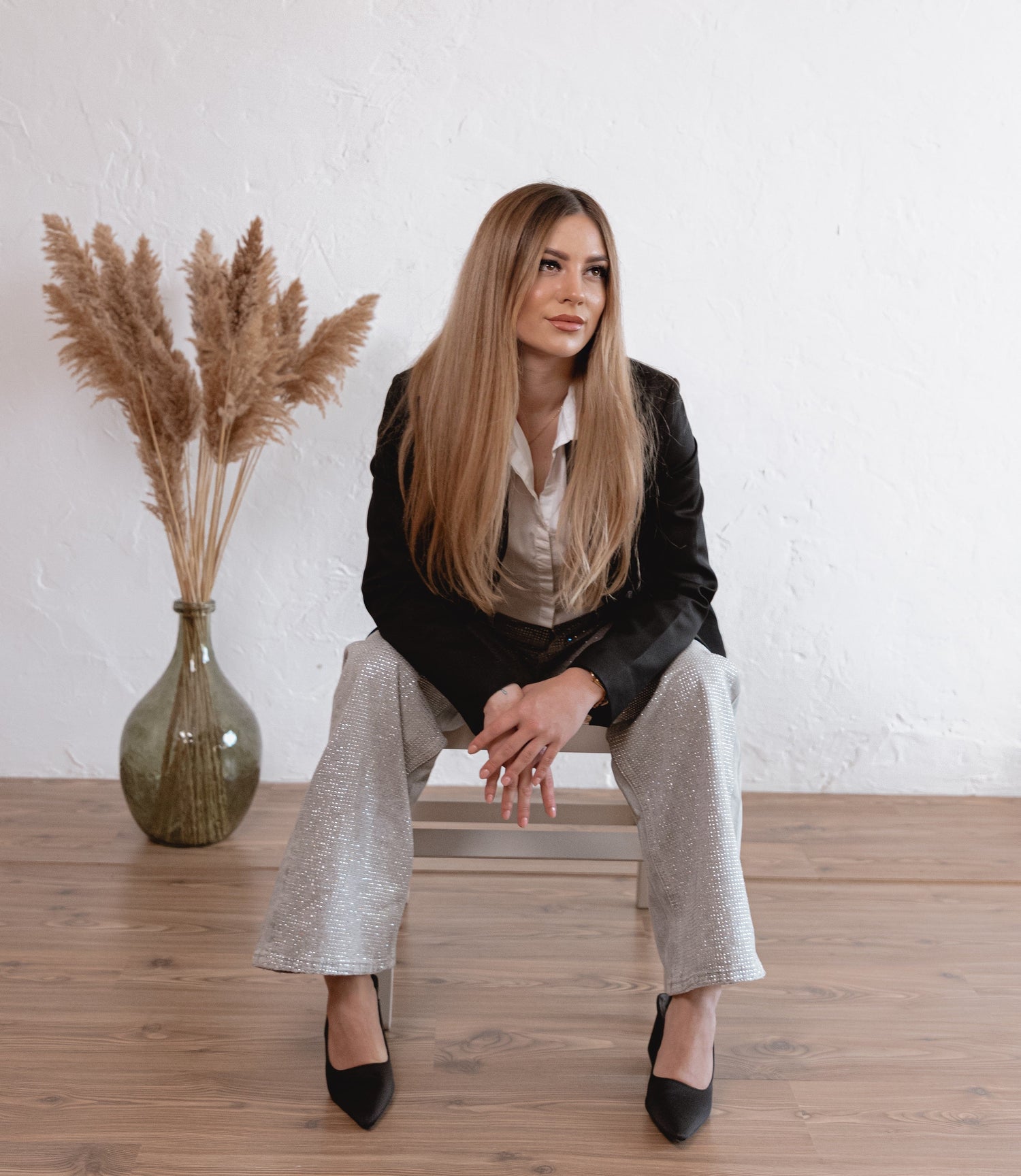 Woman sitting on a wooden floor with a vase of pampas grass in the background